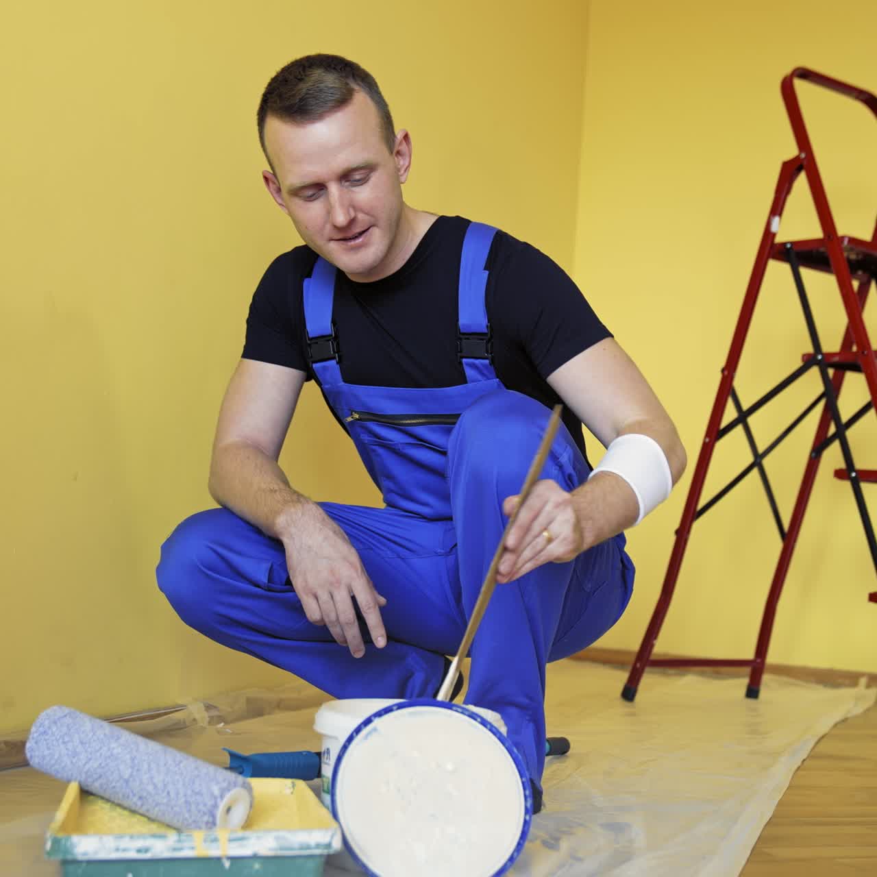 Riparazione e decorazione delle pareti in casa. Operaio in tuta blu che prepara il colore prima di dipingere le pareti nella stanza. Muratore che lavora al chiuso. Rinnovamento a casa.