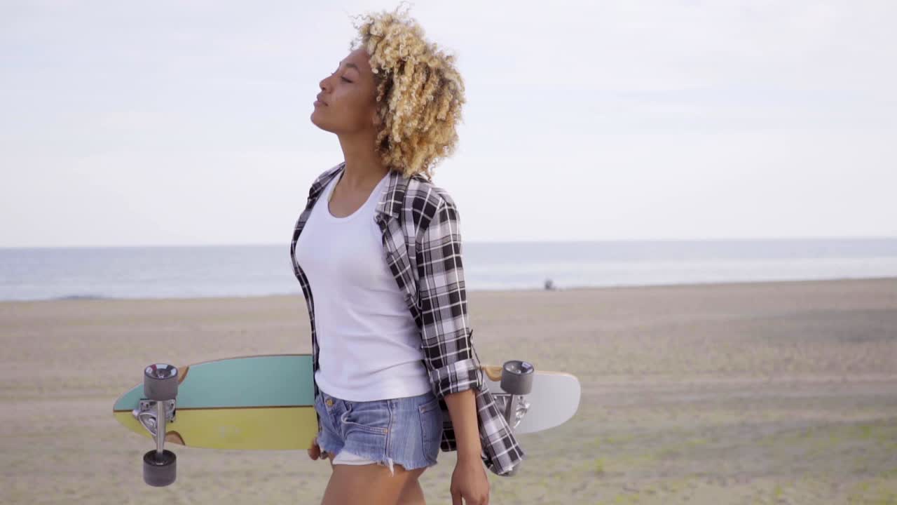 Joven mujer llevando una patineta en una playa