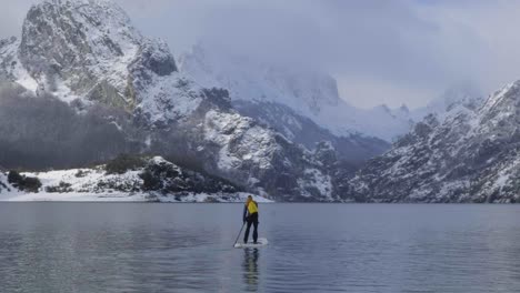 man on paddle board between water and mountains on coast