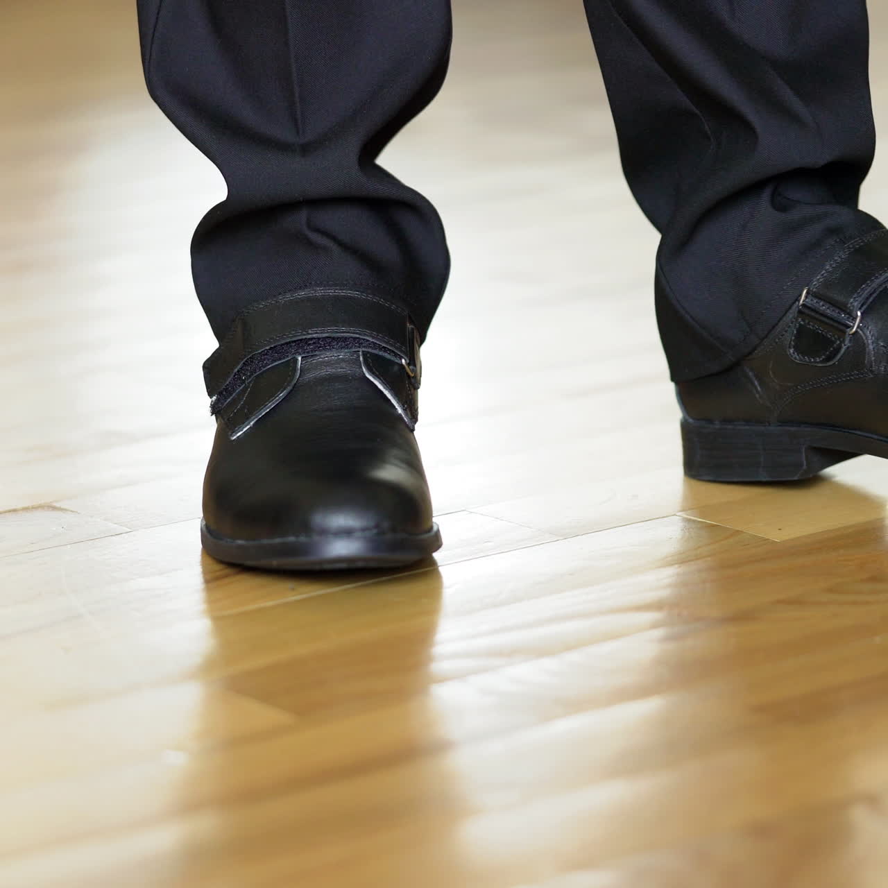 Man's legs shows black shoes standing on heels and goes away on the wooden floor. Legs of a young man in the dancing shoes. Close-up