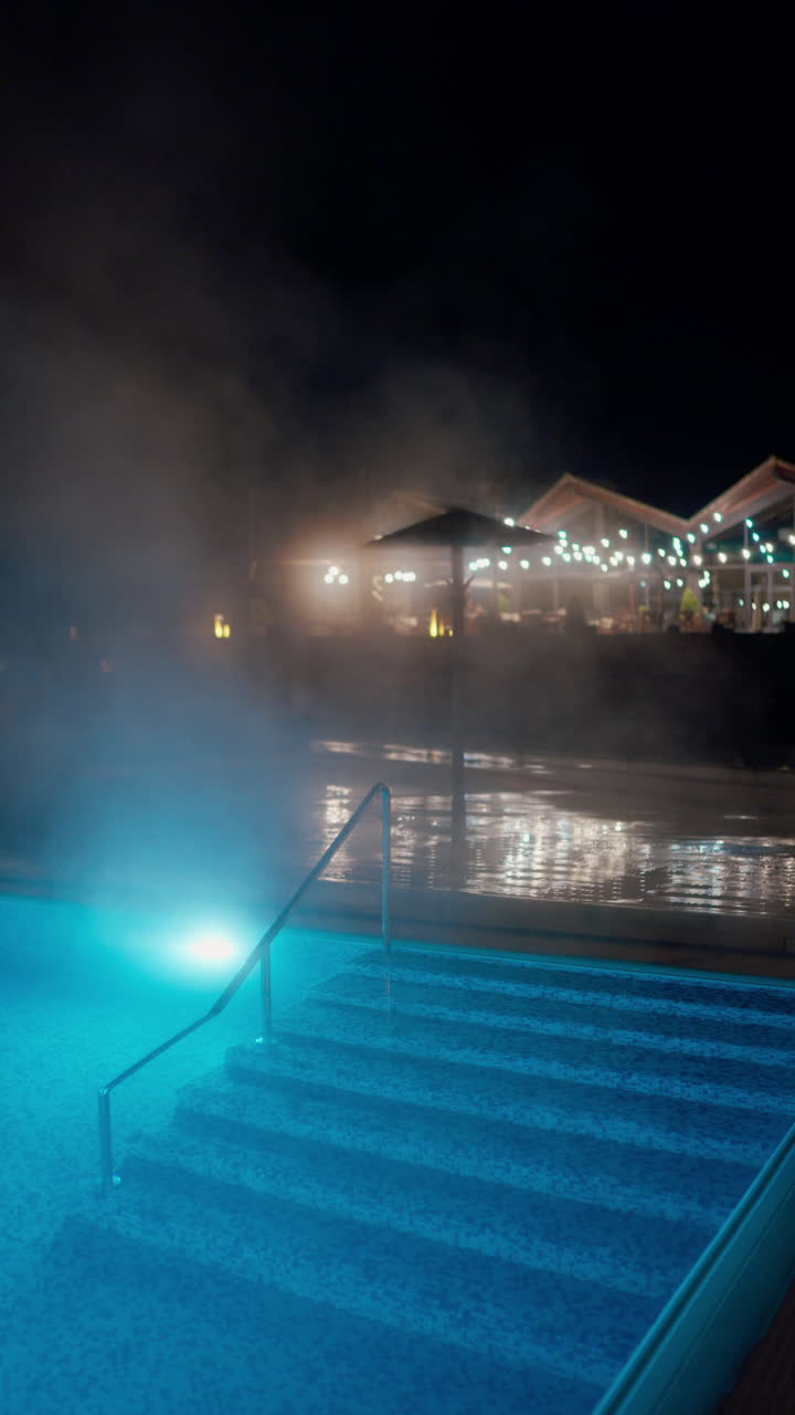 Serene Outdoor Swimming Pool with Steam and Blue Lights at Night