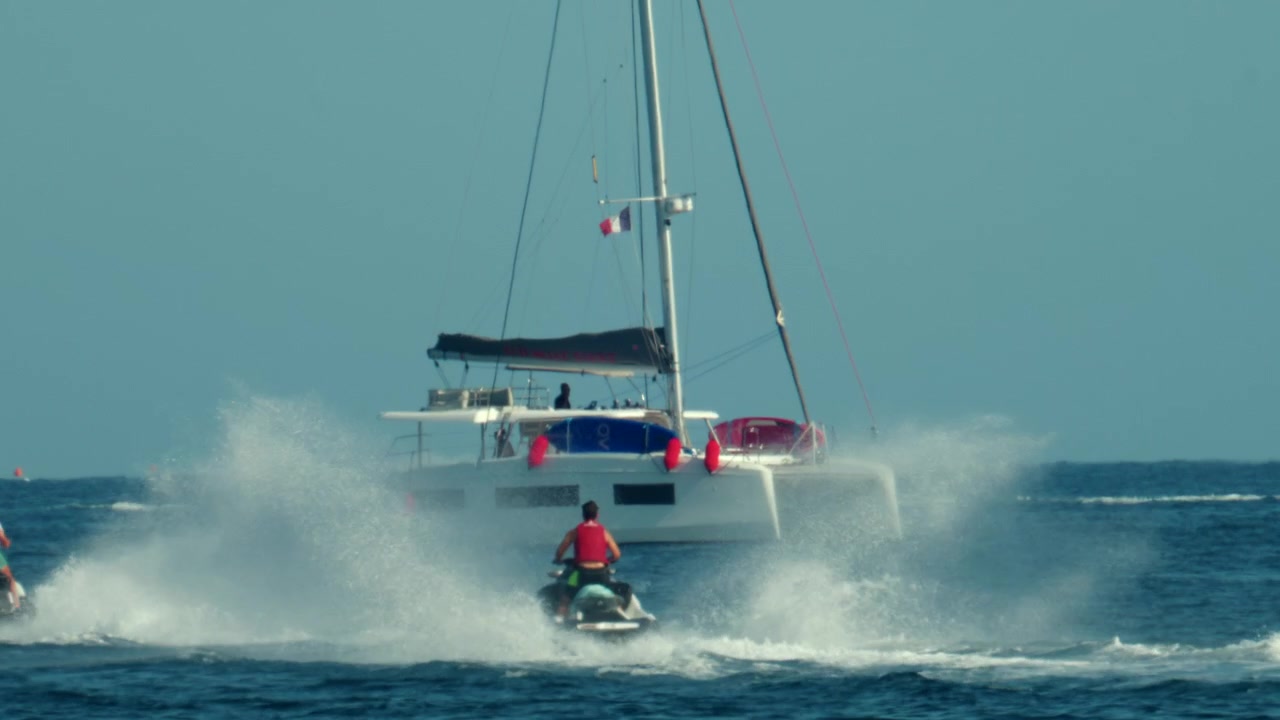 Persone che guidano moto d'acqua creando spruzzi vicino a un catamarano nell'oceano, mostrando sport acquatici e attività ricreative estive, Antibes, Francia.