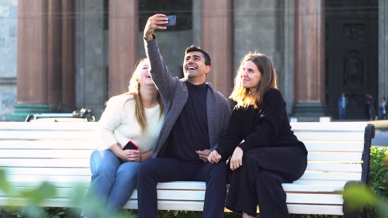 amigos tomando selfies en un banco en la ciudad