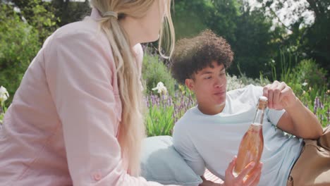 Happy-diverse-couple-having-picnic-in-garden-on-sunny-day