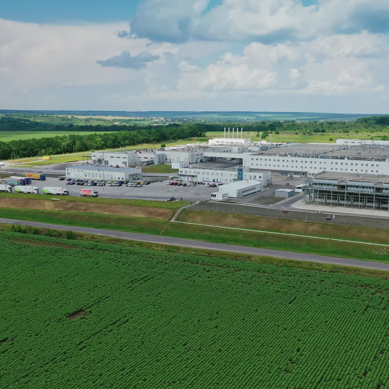 Industrial complex among nature. Modern manufacturing on beautiful green landscape. Aerial view. Motion camera back.
