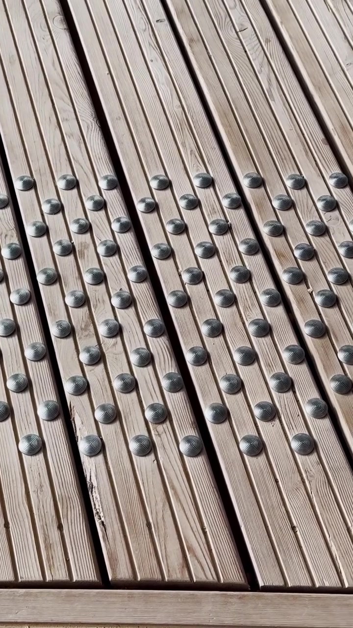 Vertical close-up of wooden tactile paving with raised metal studs, showing accessibility warning texture and clean outdoor walkway detail.