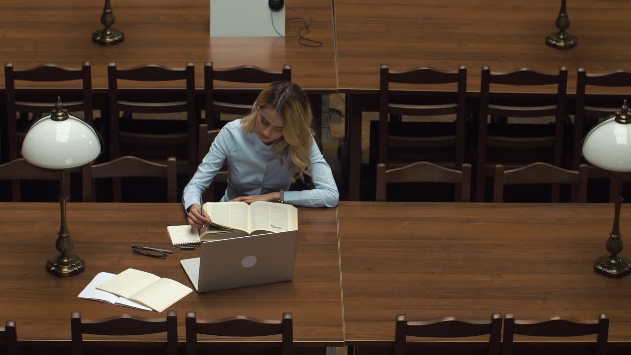 Woman reading in library with laptop