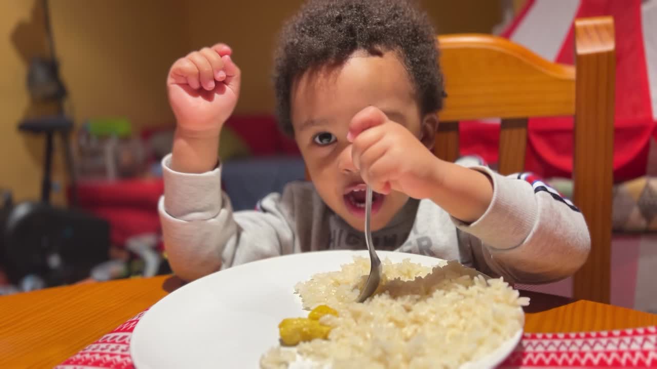 Bambino di due anni, adorabile e di origini miste, che mangia riso da solo a casa