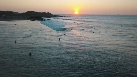 Vista-Aérea-De-Drones,-Puesta-De-Sol-En-El-Océano-Pacífico-Y-Surfistas-Esperando-Las-Olas-Junto-A-La-Costa-En-Perú