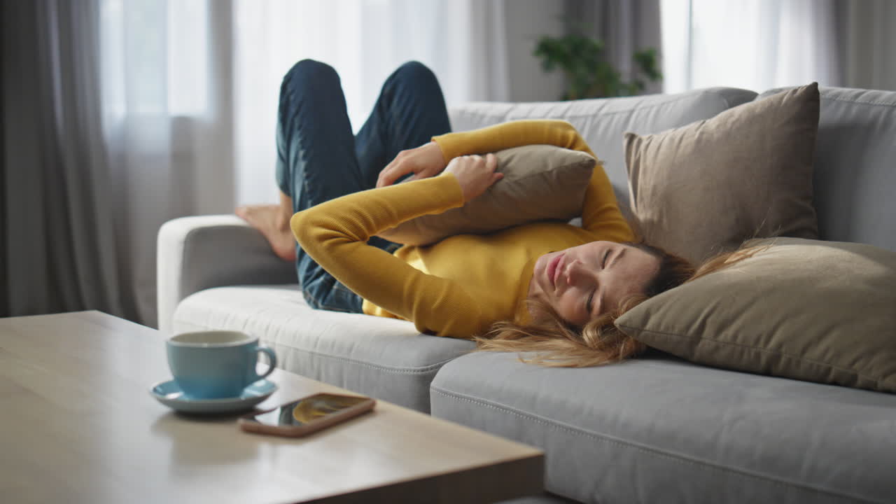 Carefree girl falling coach embracing pillow. Lady laying checking mobile phone