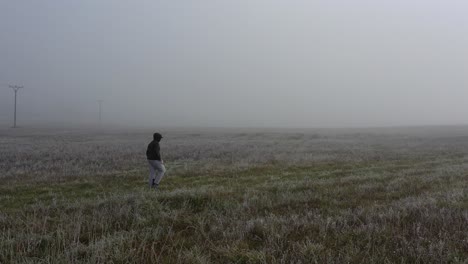 lonely man walking on meadow on foggy morning, tracking drone aerial view