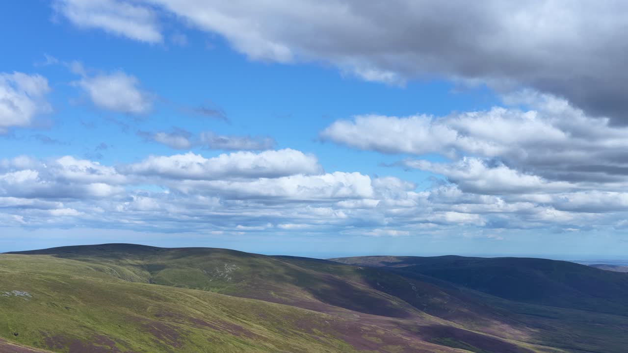 Drone camera smoothly pans across tranquil Scottish Highlands landscape with heather, hills, and scattered clouds