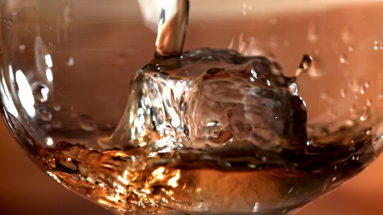 Versamento al rallentatore di whisky dorato su un cubetto di ghiaccio
