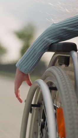 hand of little girl turning large wheel of medical equipment on blurred background. junior schoolgirl sits in wheelchair moving on pavement closeup