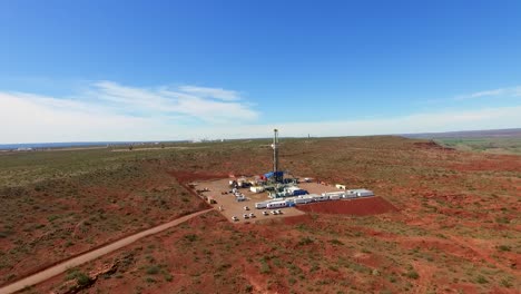 Un-Sitio-De-Fracking-En-Un-Vasto-Y-árido-Paisaje-Bajo-Un-Cielo-Azul-Claro,-Con-Maquinaria-Y-Vehículos,-Vista-Aérea