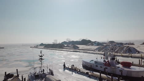 Drone-shot-of-boats-in-a-frozen-harbour-and-stone-quarry-along-lake-erie-in-Ontario,-Canada-in-the-middle-of-winter