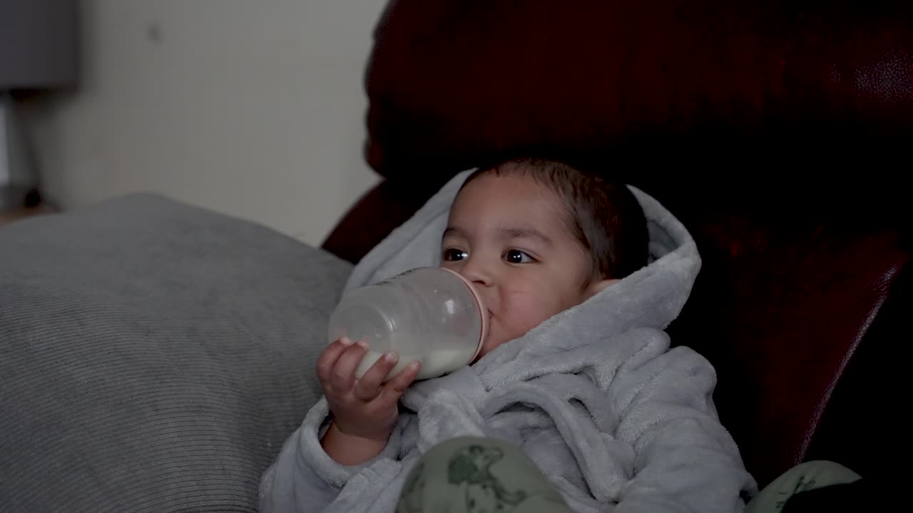 Bambino piccolo carino che beve latte mentre è sdraiato.