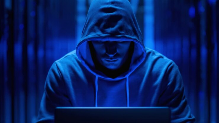 Una figura misteriosa con una felpa incappucciata impegnata in intriganti attività digitali all'interno di una sala server oscurata e immersa in una luce blu.