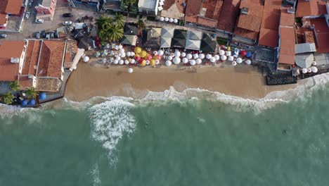 Luftdrohnenaufnahme-Aus-Der-Vogelperspektive-Des-Wunderschönen-Tropischen,-Berühmten-Pipa-Strands-Bei-Flut-Mit-Touristen,-Die-An-Einem-Sommerabend-Im-Wasser-Spielen-Und-Den-Schatten-Unter-Bunten-Sonnenschirmen-Genießen