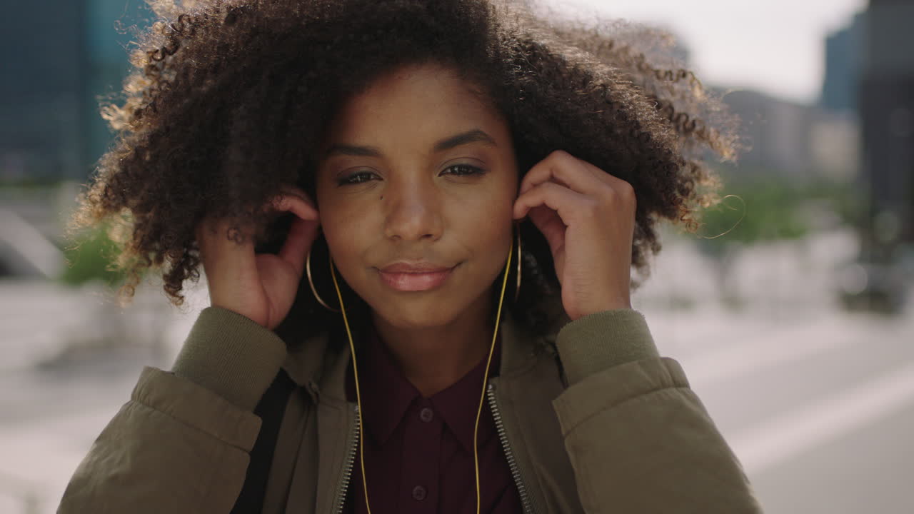 retrato en primer plano de una joven moderna mujer afroamericana estudiante con auriculares escuchando música sonriendo con confianza ante la cámara disfrutando del estilo de vida universitario urbano