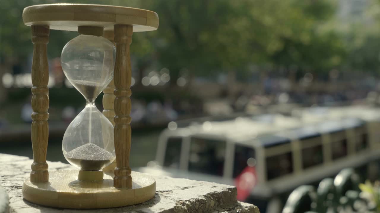 Time running out with sand in hourglass, defocused passenger ship in river