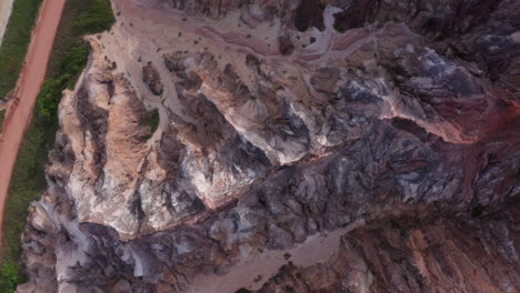 aerial - dirt road and red cliffs at falesias do gunga beach, alagoas, brazil, top down