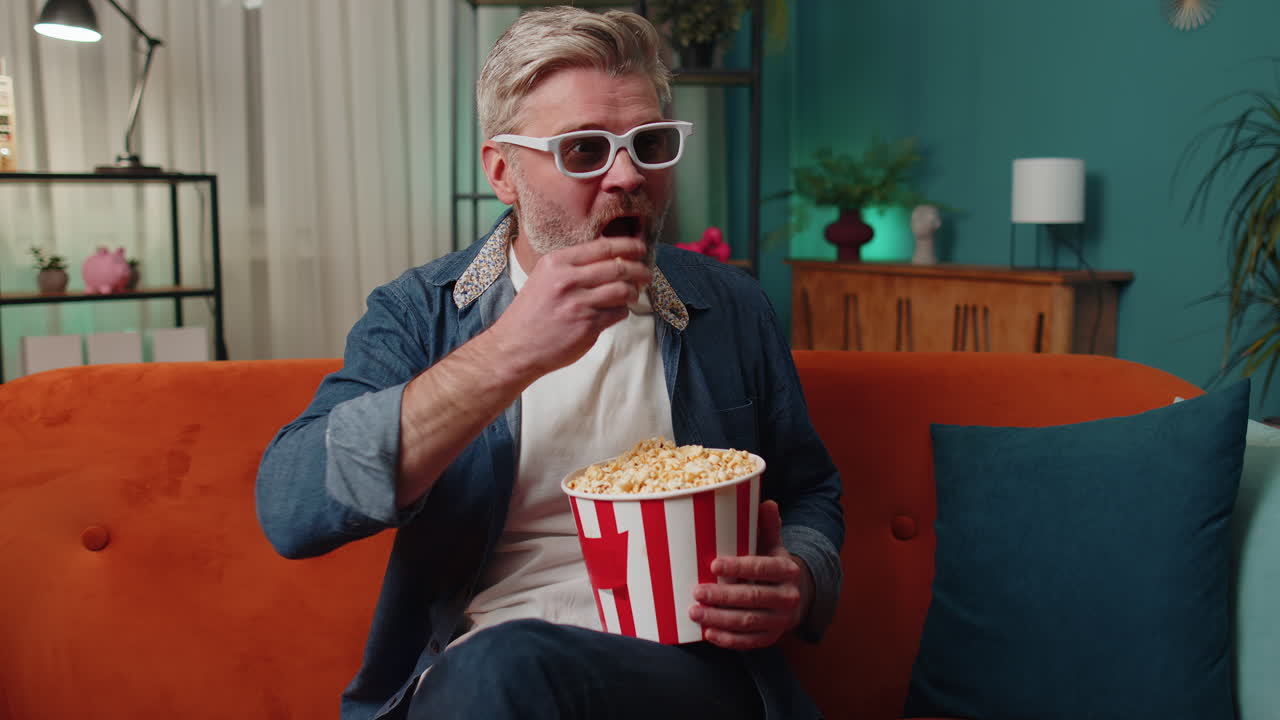 hombre sentado en el sofá comiendo palomitas de maíz y viendo interesantes series de televisión, juegos deportivos en línea en casa