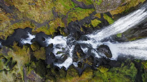 agua de la cascada que cae sobre las rocas y fluye río abajo con la orilla del río cubierta de musgo