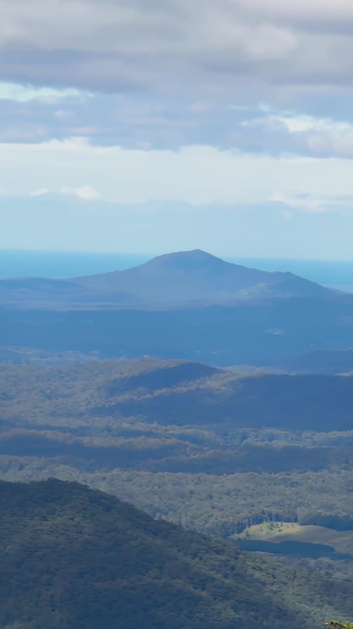 Fejende luftpanorama om dagen afslører frodige skovklædte Dorrigo-bjergkæder i New South Wales, Australien, afsluttende med fjern havhorisont under delvist skyet himmel