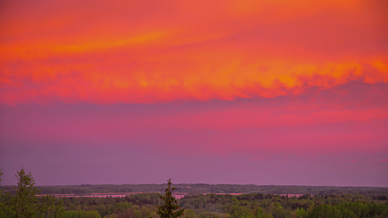 un amanecer naranja bajo una cubierta de nubes sobre un paisaje con bosque y río