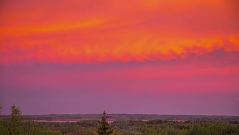 an orange sunrise under a cloud cover over a landscape with forest and river