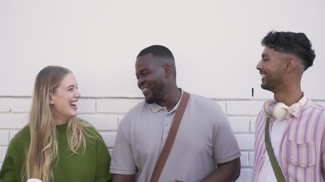 Diverse friends laughing while center man entering frame, chatting, holding coffee on sidewalk