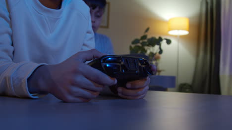 Nahaufnahme-Der-Hände-Von-Zwei-Kleinen-Jungen-Zu-Hause,-Die-Spät-In-Der-Nacht-Mit-Einer-Computerspielkonsole-Im-Fernsehen-Spielen-Und-Controller-Halten