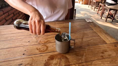 person pouring soda over ice in a glass