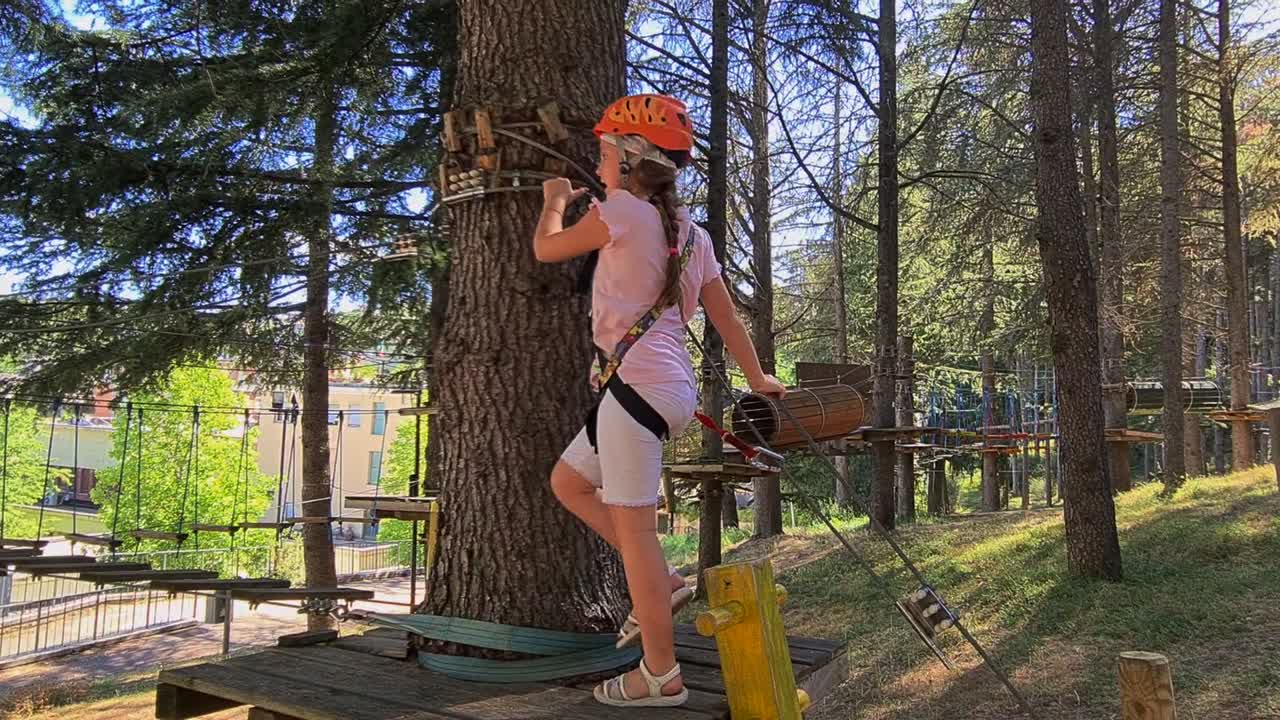 모험을 좋아하는 여자 아이가 키즈 로프 어드벤처 파크에 올라갑니다.