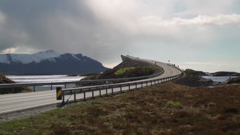 a view of the famous atlantic road in norway. one of its' curved bridges rises above the sea. the white-gray mass of clouds hanging above. blue sky on the other side of the road