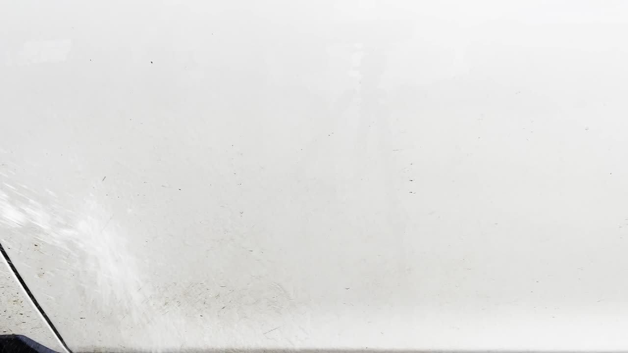 강력한 호스를 사용하여 물로 흰색 차에 먼지와 진흙 층을 분사합니다.