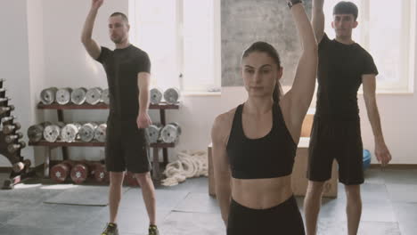 a strong and athletic young woman and two young men doing stretching exercises in the gymnasium