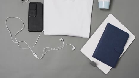 Vídeo-De-Camiseta-Blanca,-Cuadernos,-Teléfonos-Inteligentes-Y-Auriculares-Con-Espacio-Para-Copiar-Sobre-Fondo-Gris