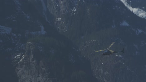 blue helicopter flying towards through snow capped mountains in slow motion 4k footage