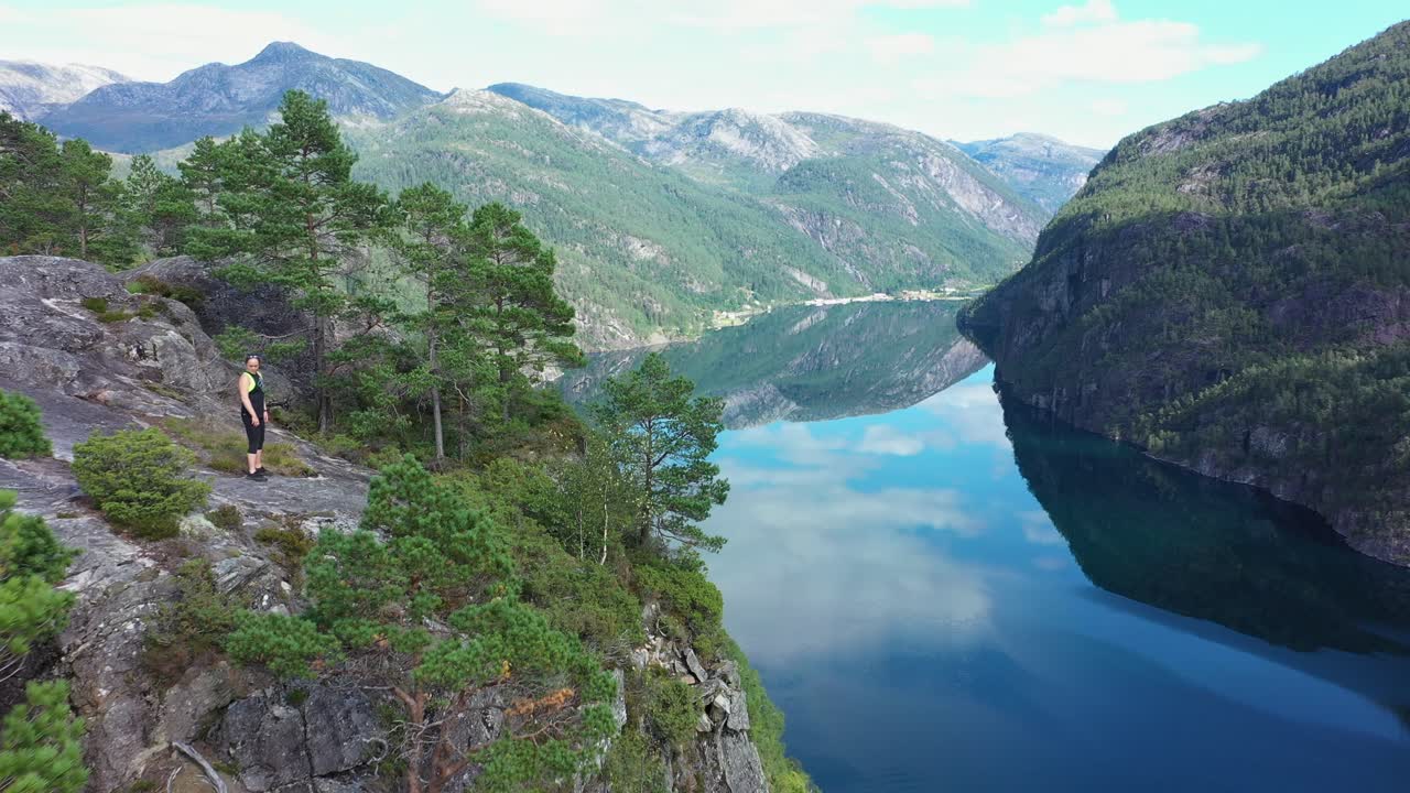 Woman standing on edge of tall cliff with panoramic view of Mo fjord and mesmerizing mountain landscape - Norway aerial