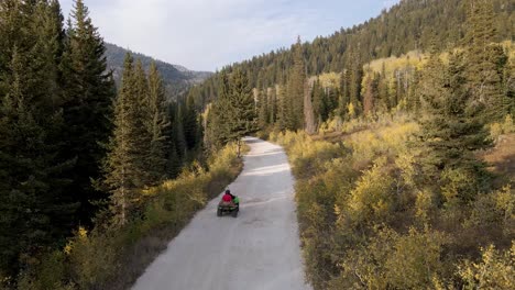 all terrain vehicle atv on mountain backcountry road, rear aerial view