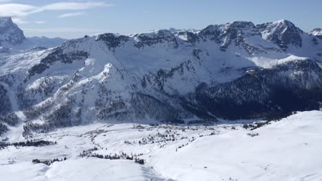 Panoramic-drone-shot-of-beautiful-snowy-Italian-mountain-range-during-sunny-weather-with-blue-sky-and-some-clouds