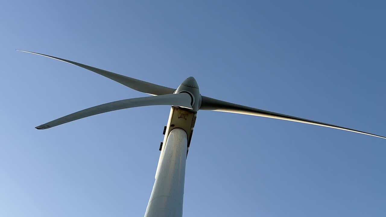 Close view of a white wind turbine from bellow with a blue sky