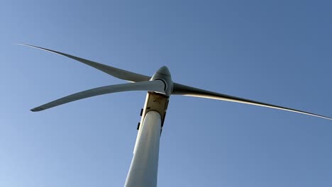 close view of a white wind turbine from bellow with a blue sky