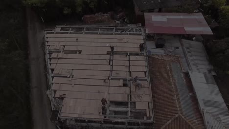 dolly en la placa de techo de una estructura de dos pisos, sobre ella se encuentran algunos trabajadores, este lugar está rodeado de árboles y un pequeño camino a un lado.