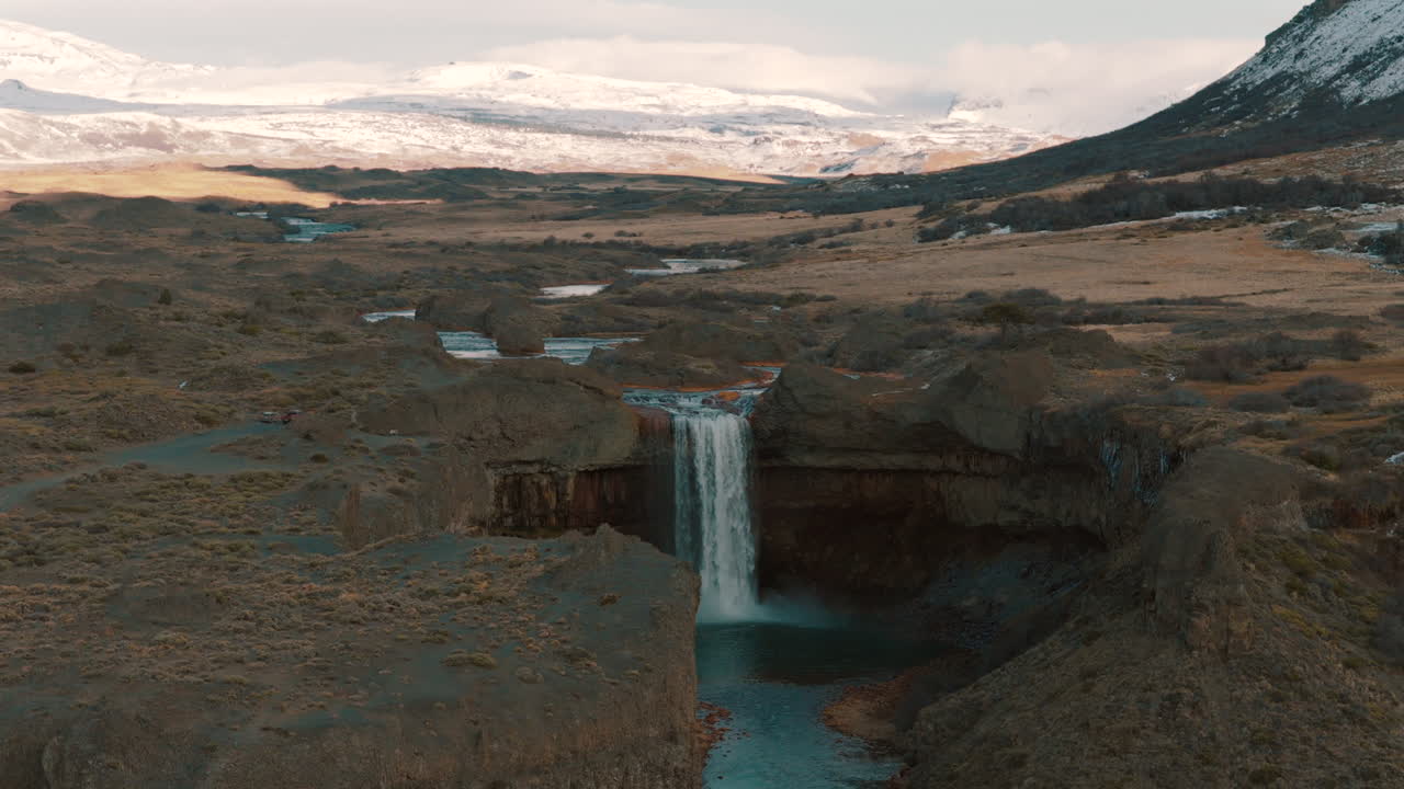 Drone view of Salto del Agrio waterfall surrounded by volcanic cliffs and snowy Andes mountains, Caviahue, Argentina