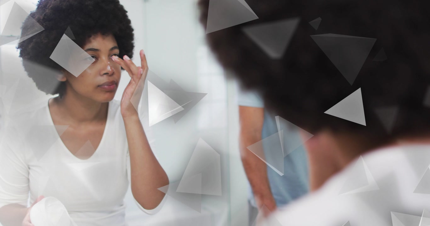 woman picking up jar and applying under-eye beauty cream for hydration in mirror, partner behind