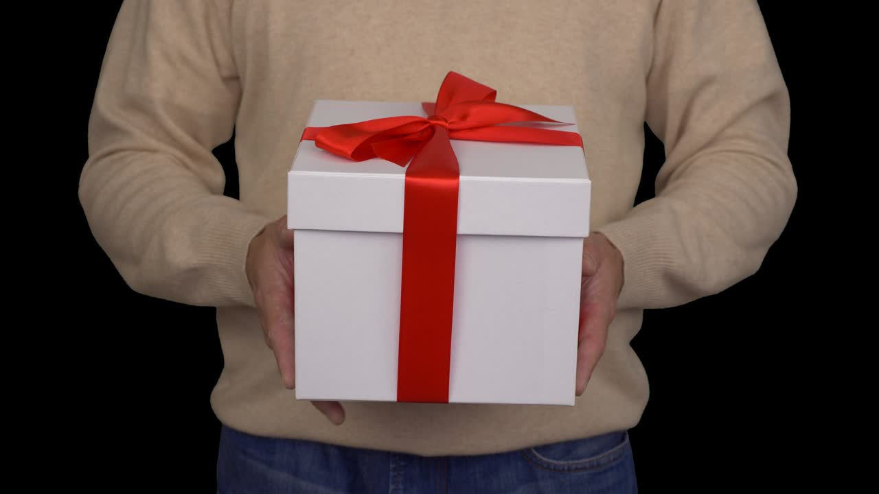 Caucasian man in beige sweater is holding a white gift box in hands. White gift box with red ribbon bow. Front view of man in casual beige sweater. Man gives a gift. Alpha channel chroma key.