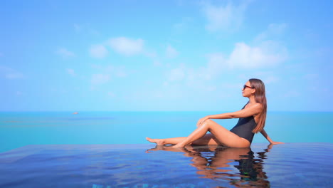 Slender-Woman-in-Swimsuit-in-Blue-Tropical-Paradise,-Infinity-Swimming-Pool,-Turquoise-Ocean-and-Blue-Summer-Sky